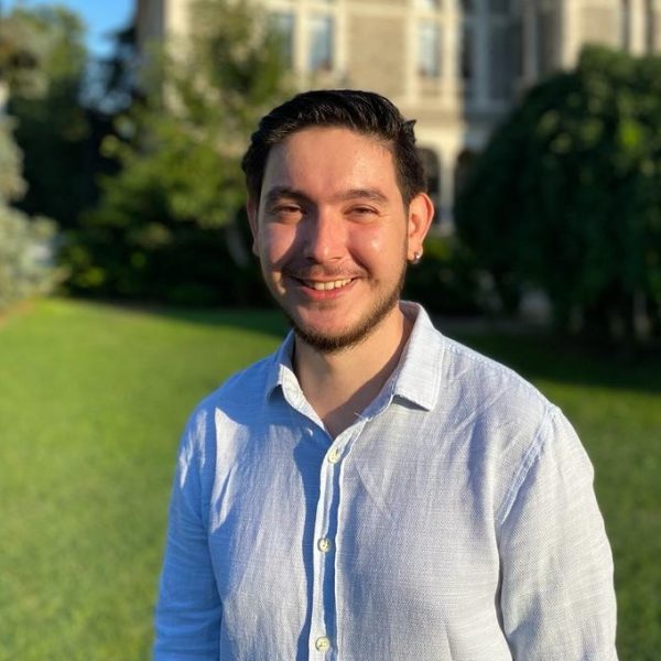 EPS PhD student Aydın Kaan Şenel smiling in front of a building outside