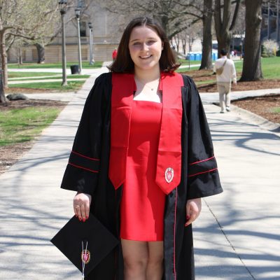 Graduating Education Studies major Elizabeth Preboski standing, smiling on Bascom Hill in a UW graduation gown with cap in hand.